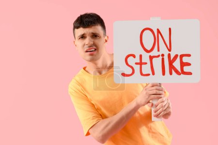 Téléchargez les photos : Manifestation d'un jeune homme tenant une pancarte avec le texte ON STRIKE sur fond rose - en image libre de droit