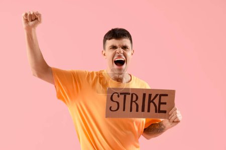 Photo for Protesting young man holding placard with word STRIKE against pink background - Royalty Free Image