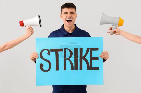 Protesting mechanic holding placard with word STRIKE and megaphones on light background