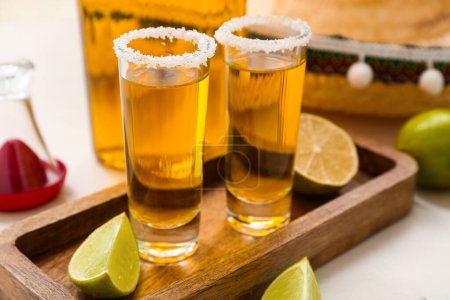 Foto de Botella de tequila con chupitos y rodajas de lima sobre fondo blanco, primer plano - Imagen libre de derechos