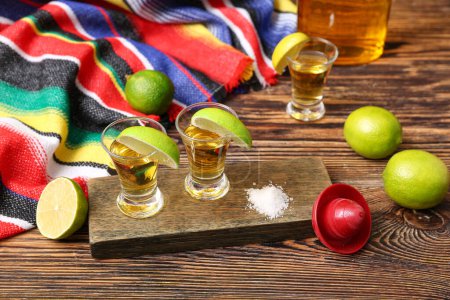 Shots of tequila with slices of lime and salt on wooden background