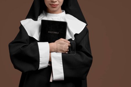 Young nun with Bible on brown background, closeup