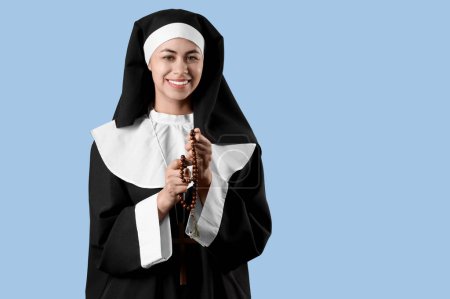 Young nun with rosary beads on blue background