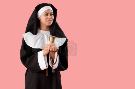 Young nun with beads and chalice on pink background