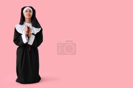 Young nun with beads praying on pink background