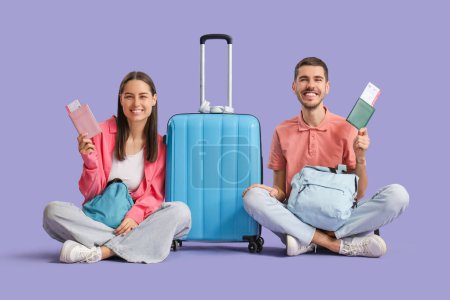 Photo for Beautiful young happy couple of tourists with suitcase, backpacks and passports on purple background - Royalty Free Image