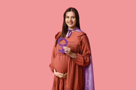 Téléchargez les photos : Belle jeune femme enceinte en cape de super-héros avec symbole de genre sur fond rose - en image libre de droit