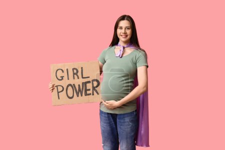 Téléchargez les photos : Belle jeune femme enceinte en cape de super-héros tenant du carton avec texte GIRL POWER sur fond rose - en image libre de droit