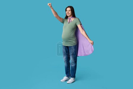Téléchargez les photos : Belle jeune femme enceinte en cape de super-héros sur fond bleu - en image libre de droit