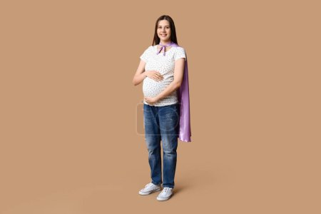 Téléchargez les photos : Belle jeune femme enceinte en cape de super-héros sur fond brun - en image libre de droit