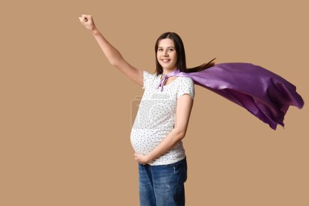 Téléchargez les photos : Belle jeune femme enceinte en cape de super-héros sur fond brun - en image libre de droit