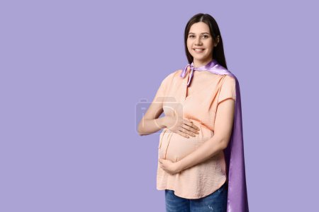 Téléchargez les photos : Belle jeune femme enceinte en cape de super-héros sur fond lilas - en image libre de droit