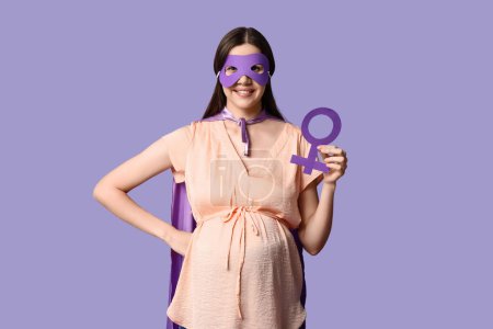 Téléchargez les photos : Belle jeune femme enceinte en costume de super-héros avec symbole de genre sur fond lilas - en image libre de droit