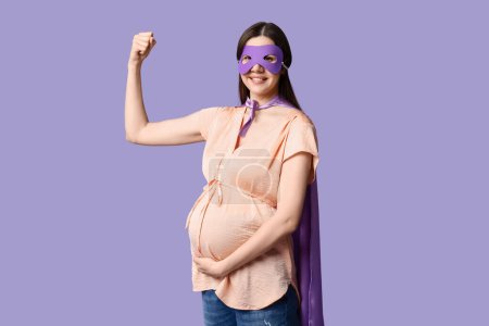 Téléchargez les photos : Belle jeune femme enceinte en costume de super héros montrant les muscles sur fond lilas - en image libre de droit