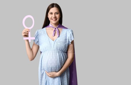 Téléchargez les photos : Belle jeune femme enceinte en cape de super-héros avec symbole de genre sur fond gris - en image libre de droit