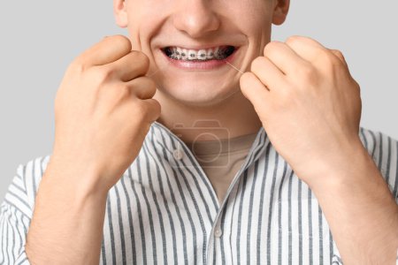Téléchargez les photos : Jeune homme avec des appareils dentaires soie dentaire dents sur fond clair, gros plan - en image libre de droit