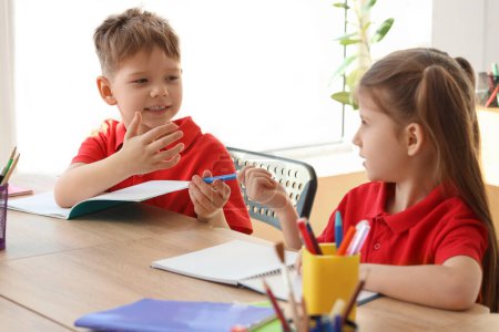 Photo for Cute little pupils writing at table in classroom. School holidays concept - Royalty Free Image