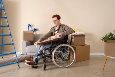 Téléchargez les photos : Jeune homme en fauteuil roulant emballage peinture lors de la réparation à la maison - en image libre de droit