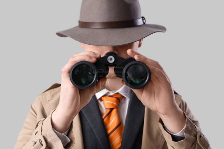 Male spy looking through binoculars on light background, closeup