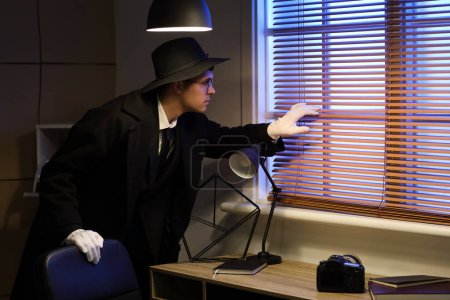 Téléchargez les photos : Homme espion regardant par la fenêtre dans le bureau la nuit - en image libre de droit