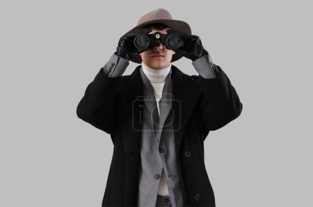 Téléchargez les photos : Homme espion regardant à travers les jumelles sur fond clair - en image libre de droit