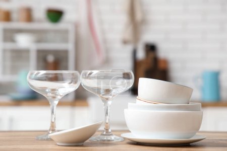 Téléchargez les photos : Empilement de vaisselle blanche et de verres propres sur une table en bois dans la cuisine - en image libre de droit