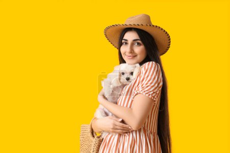 Young happy woman in hat holding her adorable Bolognese dog on yellow background