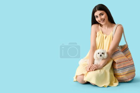 Jeune femme heureuse avec son chien bolognais mignon et son sac sur fond bleu
