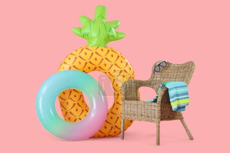 Inflatable rings and straw chair with snorkeling mask and towel on pink background