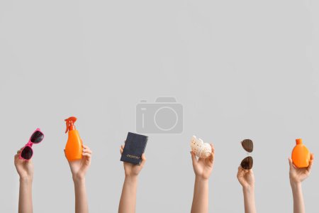 Female hands with sunglasses, passport, sunscreens and seashell on grey background. Travel concept.