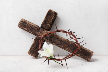 Croix en bois, couronne d'épines et de lis sur table à grunge près du mur blanc