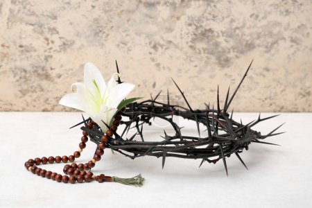 Foto de Corona de espinas con lirio y perlas de oración en mesa blanca cerca de la pared de luz - Imagen libre de derechos