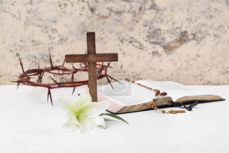 Lirio, Santa Biblia, corona de espinas y cruz sobre mesa blanca cerca de pared clara