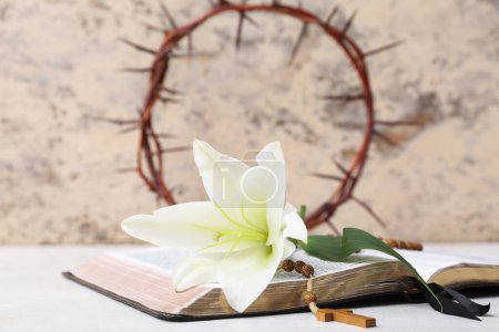 Lily, Holy Bible and crown of thorns on white table near light wall
