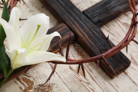 Crown of thorns with white lily and cross on wooden background, closeup