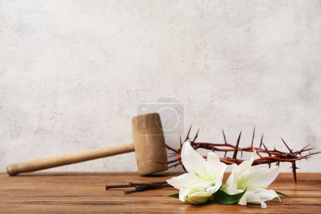Lilies, nails, crown of thorns and hammer on wooden table near light wall