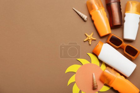 Paper sun figure, seashells, sunglasses and bottles of sunscreen cream on brown background