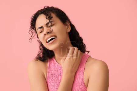 Foto de Joven mujer afroamericana con alergia a la piel arañándose sobre fondo rosa - Imagen libre de derechos