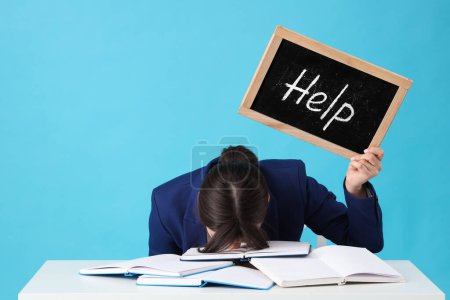 Young stressed businesswoman holding chalkboard with word HELP on blue background. Stress Awareness Month