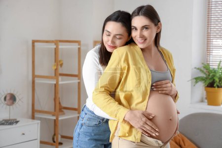 Young lesbian woman hugging her pregnant wife at home