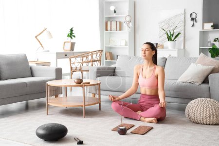 Sportliche junge Frau mit Sadhu-Brett und Aromastab beim Meditieren zu Hause