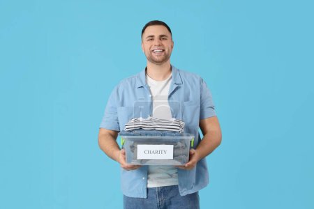 Téléchargez les photos : Jeune homme tenant boîte avec des vêtements de charité sur fond bleu - en image libre de droit