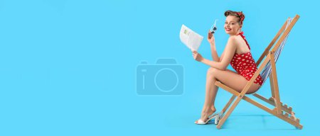 Young pin-up woman with newspaper sitting on deck chair against blue background with space for text