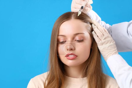 Photo for Young woman with hair loss problem receiving injection on blue background - Royalty Free Image