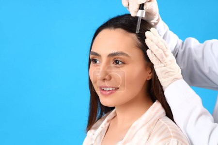 Photo for Cosmetologist applying serum on woman's hair against blue background - Royalty Free Image