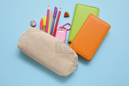 Foto de Caja de lápiz beige con diferentes artículos de papelería de la escuela y cuadernos sobre fondo azul - Imagen libre de derechos