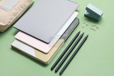 Foto de Caja de lápiz beige con diferentes artículos de papelería de la escuela y cuadernos sobre fondo verde - Imagen libre de derechos