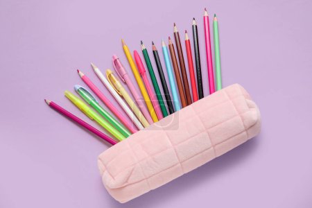 Foto de Caja de lápices con plumas y lápices de colores sobre fondo púrpura - Imagen libre de derechos