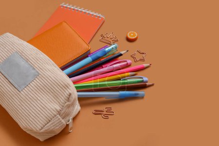 Foto de Caja de lápiz beige con diferentes artículos de papelería de la escuela y cuadernos sobre fondo marrón - Imagen libre de derechos
