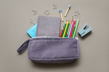 Foto de Caja de lápiz púrpura con diferentes artículos de papelería de la escuela y cuaderno sobre fondo gris - Imagen libre de derechos
